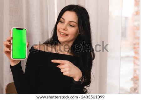 Smiling person wear casual clothes show smartphone with green chromakey screen, recommendation app promotion or mobile technology use in cafe. Online services, connectivity, ad and offer, sale.