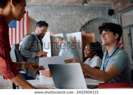 Happy volunteer assisting voters during elections at polling station. Royalty-Free Stock Photo #2433504131
