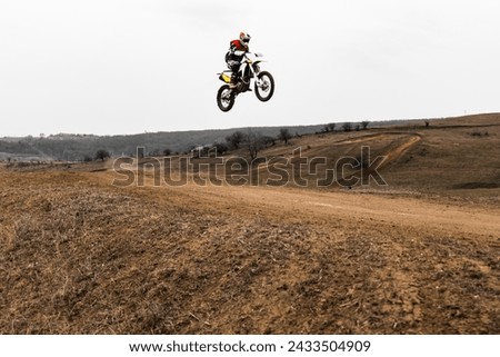 A person is airborne on a motocross dirt bike jumping with a helmet in the sky Royalty-Free Stock Photo #2433504909