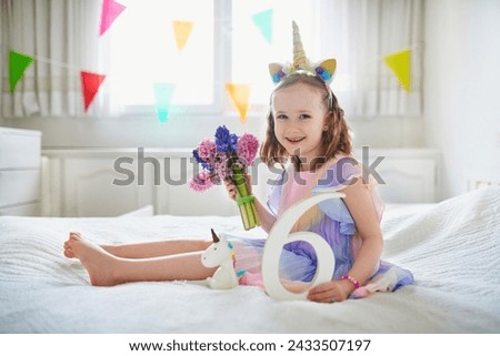 Adorable preschooler girl in red dress sitting on bed with pink hyacinths and white wooden number six. Sixth birthday concept. Kid celebrating sixth birthday Royalty-Free Stock Photo #2433507197