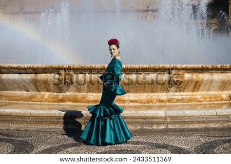 Beautiful young woman in a green frilly suit with a flower on her head. The woman is dancing flamenco and is in the most famous square in seville, spain, in front of its central fountain Royalty-Free Stock Photo #2433511369