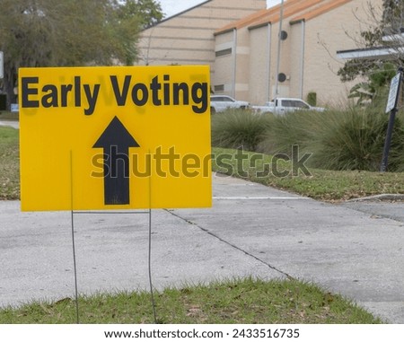 Yellow and black Early voting sign with black directional arrow on grass area by sidewalk