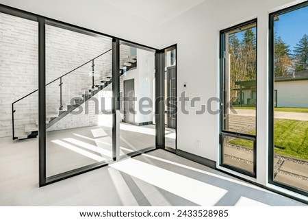 Contemporary modern home interior entry foyer with large glass and black doors a floating staircase against a painted white brick wall wrought iron bannister and railing with soft pale hardwood floors Royalty-Free Stock Photo #2433528985