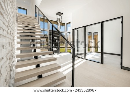 Contemporary modern home interior entry foyer with large glass and black doors a floating staircase against a painted white brick wall wrought iron bannister and railing with soft pale hardwood floors Royalty-Free Stock Photo #2433528987