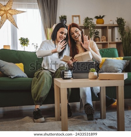 two women teenage friends or sisters receive presents in box open read card happy smile in front of digital tablet at home online video call
