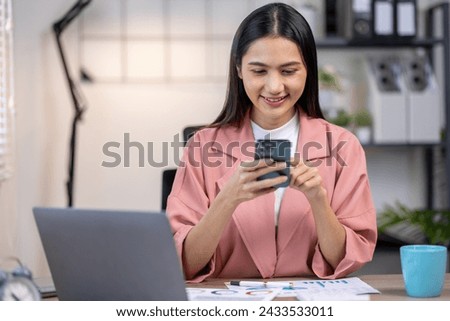 Portrait of happy young asian woman accountant working documents on laptop and  phone desk using calculator for calculate finance report in home office