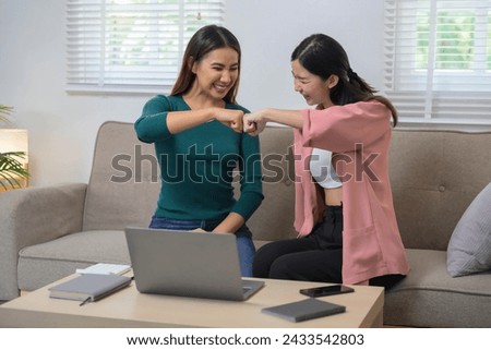 Two joyful women working together with laptop computer while sitting on the sofa, freelance, work from home concept.