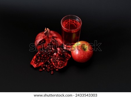 A tall glass of red fruit juice and a broken pomegranate and a ripe red apple on a black background. Close-up.