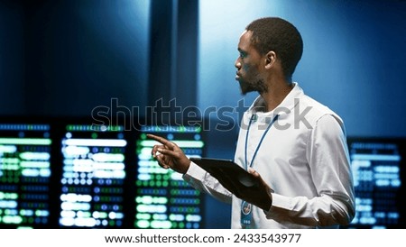 African american specialist using tablet to check data center security features protecting against unauthorized access, data breaches, DDoS attacks and other cybersecurity threats Royalty-Free Stock Photo #2433543977