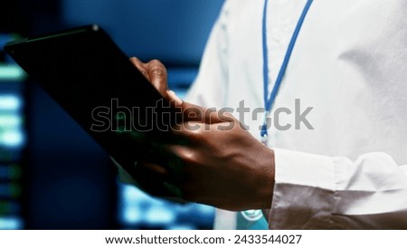 IT programmer using tablet to monitor supercomputer hub security features protecting against unauthorized access, data breaches, phishing attacks and other cybersecurity dangers, close up Royalty-Free Stock Photo #2433544027