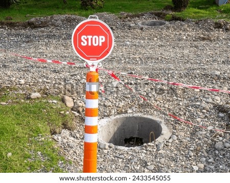 A stop sign in a park in front of an open manhole. Danger lies ahead. A lopsided sign. There is no passage. Road work concept.