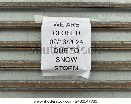 "We are closed 02 13 2024 due to snow storm" paper sign taped to a metal storefront gate in New York City