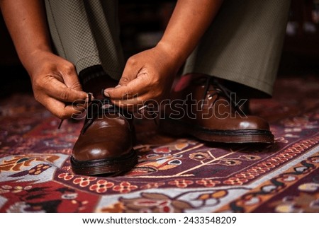 Concept photo of 3-hole boots made of genuine leather worn indoors with a classic red Turkish carpet. Men's Feet in stylish brown boots on the Turkish red carpet