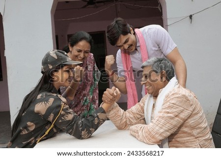 Indian female soldier and rural father playing arm wrestle together in village. Indian family playing arm wrestle and waiting who is winner?