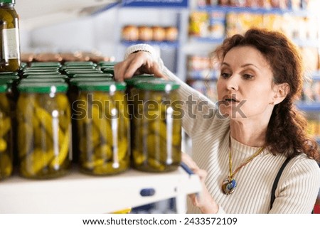 Adult female shopper in casual clothes chooses pickled cucumbers in grocery store. High quality photo