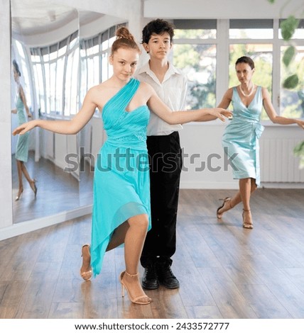 Couple of successful elegantly dressed young dancers, teenage girl and boy performing curtsy and bow after dance performance in choreography studio with female teacher in background..