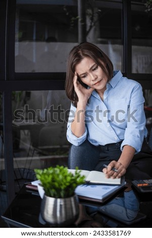 Stressed businesswomanor company employee is sitting at desk with laptop and paper works at workplace thinking, contemplating, and worrying about business matters, plans, and investment outcome  Royalty-Free Stock Photo #2433581769