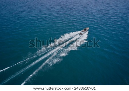 A large modern high-speed wooden luxury boat moves on blue water, top view. Expensive wooden boat, man and woman in motion on the water making a white trail looking like air. Royalty-Free Stock Photo #2433610901