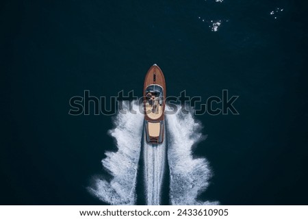 Top view of a wooden powerful motor boat. Luxurious wooden boat fast movement on dark water. A large modern high-speed wooden luxury boat. Classic Italian wooden boat fast moving aerial view. Royalty-Free Stock Photo #2433610905