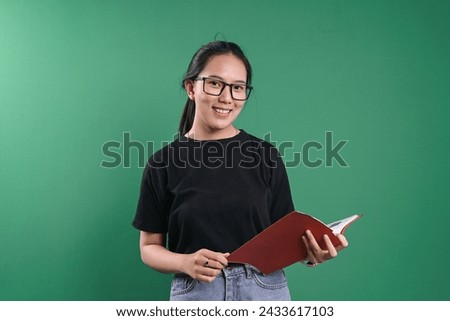 Smart Korean student woman in eyewear holding a book isolated on green background