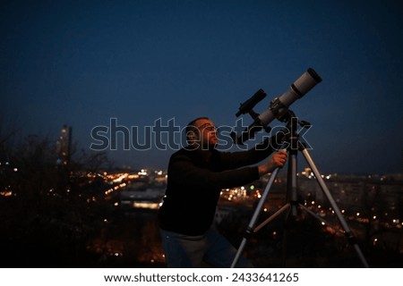 Amateur astronomer looking at the evening skies, observing planets, stars, Moon and other celestial objects with a telescope in urban city area. Royalty-Free Stock Photo #2433641265