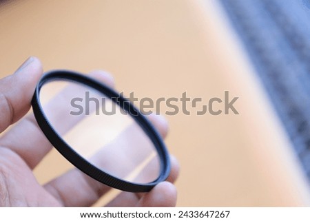 Hand puts a transparent clean protective UV filter to the camera, in the blurry yellow background