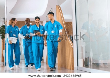 Multi Cultural Medical Team Wearing Scrubs Walking Along Corridor In Modern Hospital Royalty-Free Stock Photo #2433666965