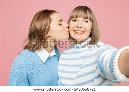 Elder parent mom with young adult daughter two women together wear blue casual clothes do selfie shot pov on mobile cell phone kiss isolated on plain pastel light pink background. Family day concept