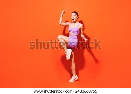 Full body sideways young fitness trainer instructor woman sportsman wear top shorts purple clothes train in home gym do winner gesture isolated on plain orange background Workout sport fit abs concept