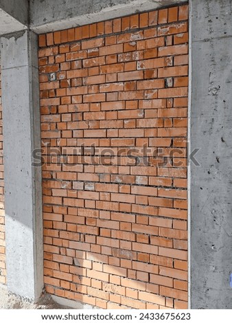 A brick wall with a cement base. The wall is made of red bricks and has a grey cement base