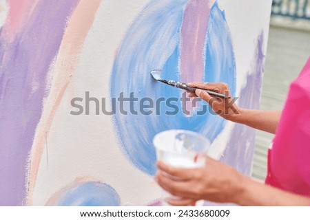 Female artist hand applies small brushstrokes of paint with paintbrush to canvas creating picture for exhibition, close up view of female hand painter creative process
