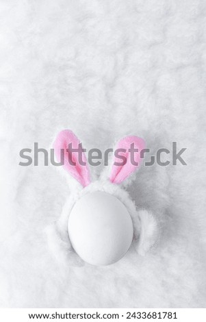Creative Easter concept. White egg with fluffy ears of Easter bunny on fluffy soft white background with copy space. 