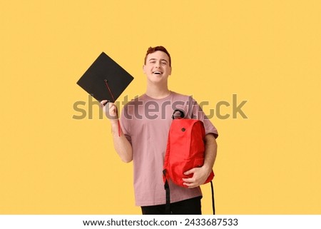 Male student with mortar board and backpack on yellow background