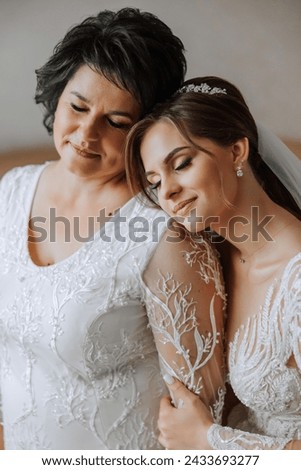 A beautiful and happy mother and her daughter, the bride, are standing next to each other. The best day for parents. Tender moments at the wedding. Royalty-Free Stock Photo #2433693277