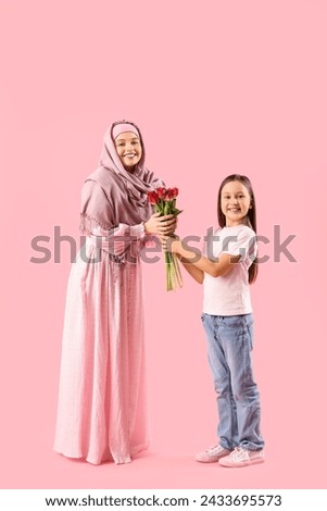 Little girl greeting her Muslim mother with tulips on pink background Royalty-Free Stock Photo #2433695573