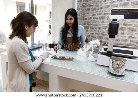 Horizontal photo a customer handpicks her favorite Arabic pastries, while the attentive shop assistant readies the elegant box for an exquisite selection. Food and culture concept. Royalty-Free Stock Photo #2433700221