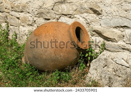 Small Kvevri or Qvevri on the grass near the stone wall.  Kvevri are earthenware vessels used for 
the fermentation, storage and ageing of traditional Georgian wine. Made from clay with a wide 
neck.  Royalty-Free Stock Photo #2433705901