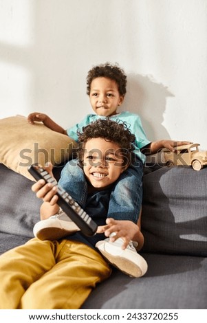 merry african american cute boys holding remote control and wooden toy car and watching movies