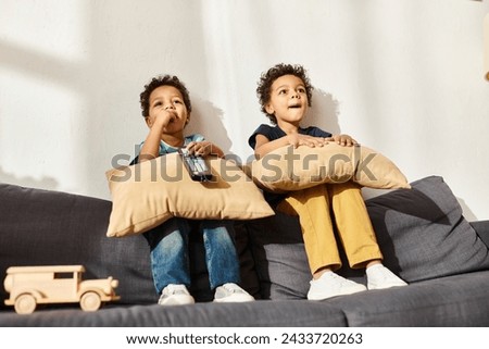 joyful african american cute brothers sitting on sofa with pillows and watching TV in living room