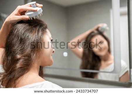 Young woman doing self hair scalp massage with scalp massager or hair brush for hair growth stimulating at home. Reflected view of the mirror. High quality photo