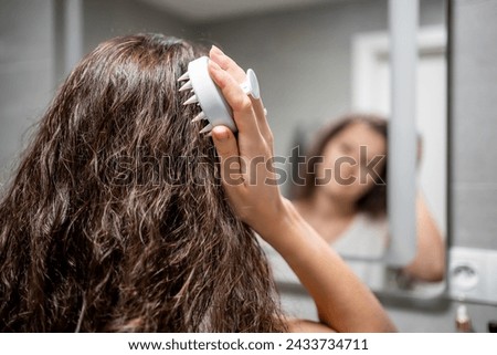 Young woman with dark curly hair doing self hair scalp massage with scalp massager or hair brush for hair growth stimulating at home. High quality photo