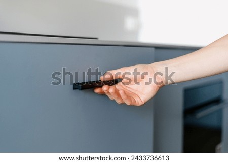 Closeup on woman hand hold black handle, open cupboard door, want to take something. Cropped view on female close kitchen cabinet. Detail in interior, modern furniture