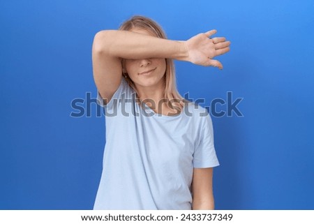Young caucasian woman wearing casual blue t shirt covering eyes with arm, looking serious and sad. sightless, hiding and rejection concept  Royalty-Free Stock Photo #2433737349