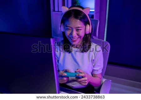 A beautiful female gamer happily plays in a private room with dim lighting that is perfect for creating a gaming mood, She has a passion for playing games, playing games is a hobby.