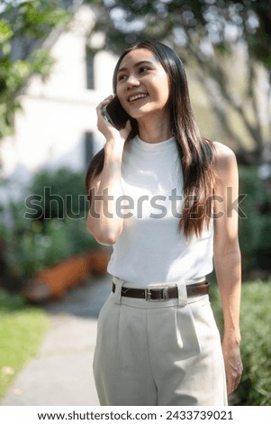Cheerful young woman walks and talking on smartphone in lush green garden