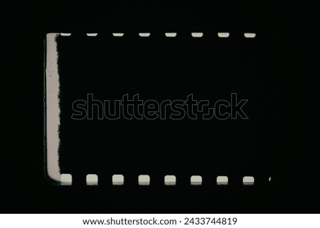 Black background with original 35mm film reel with empty dusty frames or cells and nice texture on the border, fluff on the film stock, real film grain