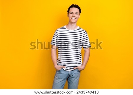 Photo of cool confident guy with stylish hairdo dressed striped t-shirt holding arms in pockets isolated on vivid yellow color background