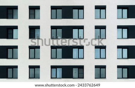 The building is tall and has many windows. The windows are mostly black and white, with some blue accents. The building appears to be a modern apartment building with a minimalist design Royalty-Free Stock Photo #2433762649