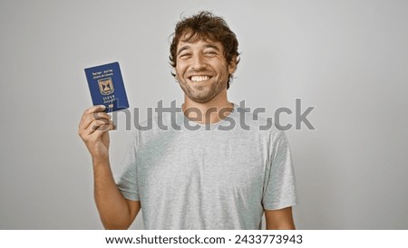Bearded, blonde, young man standing confident, flashing a joyous smile as he holds his israeli passport aloft, against a white isolated background. adult, casual, happy patriot ready for travel.