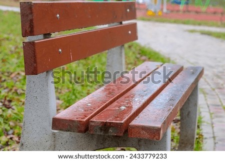 Concrete bench with seat and backrest made of boards in raindrops on a January day. Gray and colorless - like a hospital corridor - January day in a small park in the city. Royalty-Free Stock Photo #2433779233